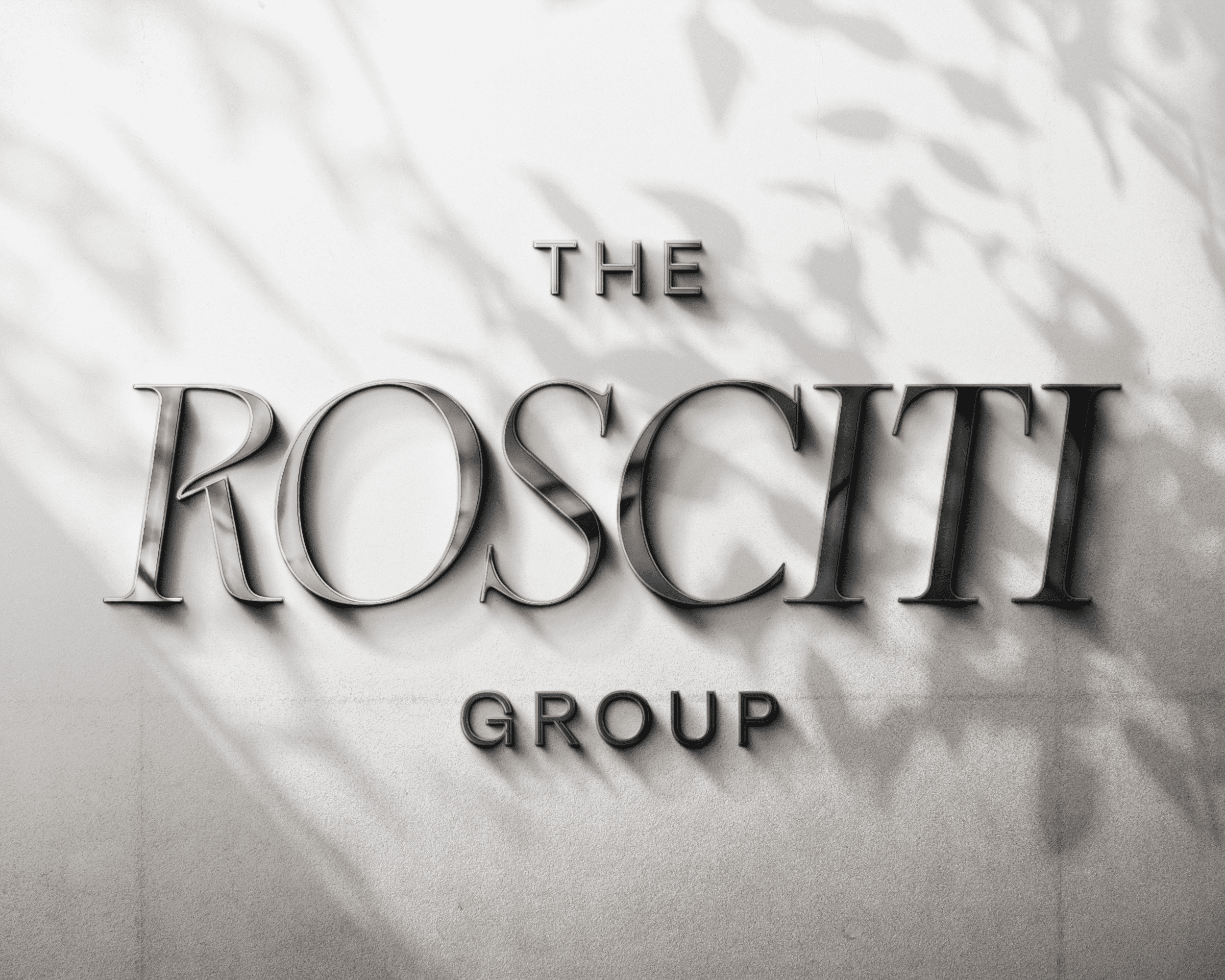 Metallic "The Rosciti Group" real estate agent logo with leaf shadows on a light background.
