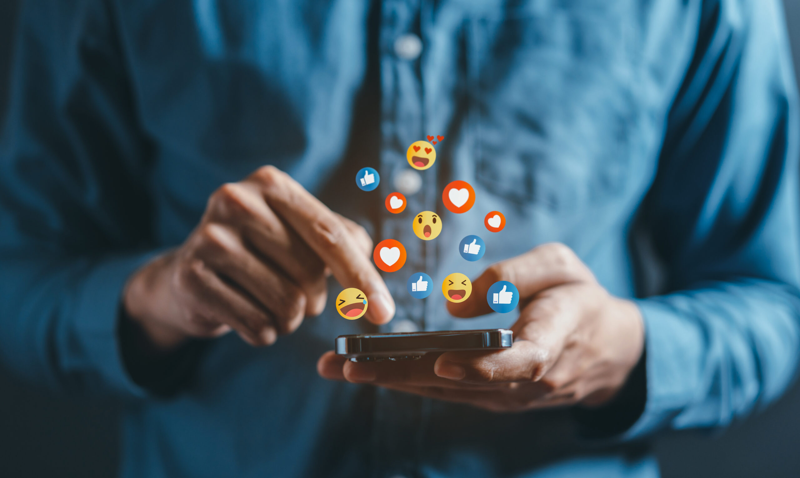 A man interacts with a smartphone, surrounded by social media reaction icons.