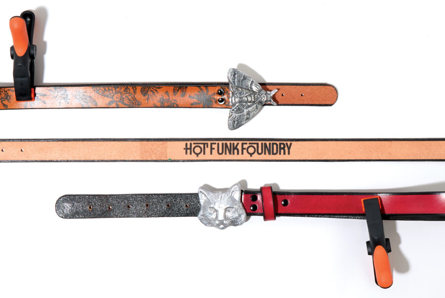 Two belts displayed flat, one with a moth buckle and the other with a cat head buckle, both labeled "Hot Funk Foundry.
