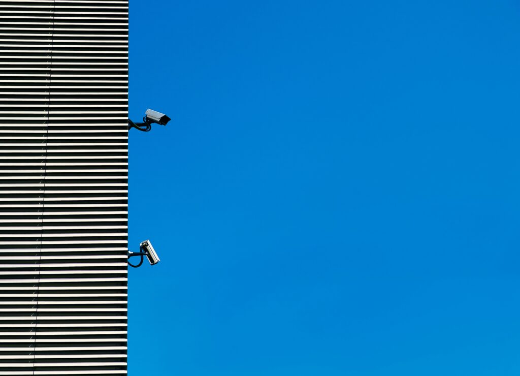 Surveillance cameras mounted on a building against a clear blue sky.