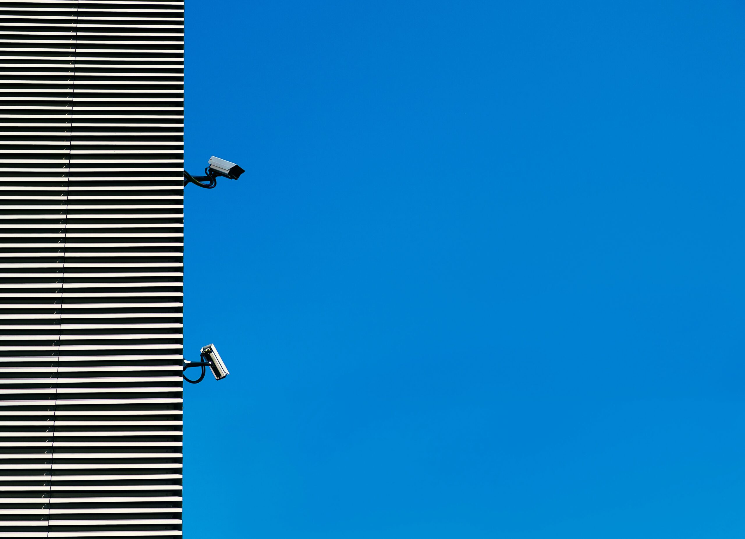 Surveillance cameras mounted on a building against a clear blue sky.
